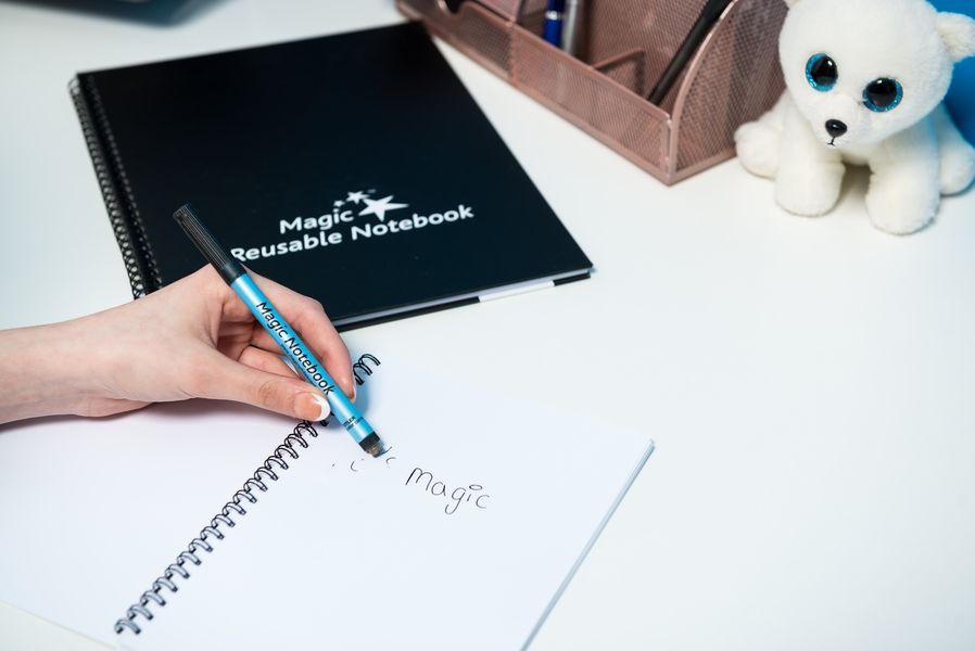 A person writing in a Magic Whiteboard reusable notebook with a blue marker